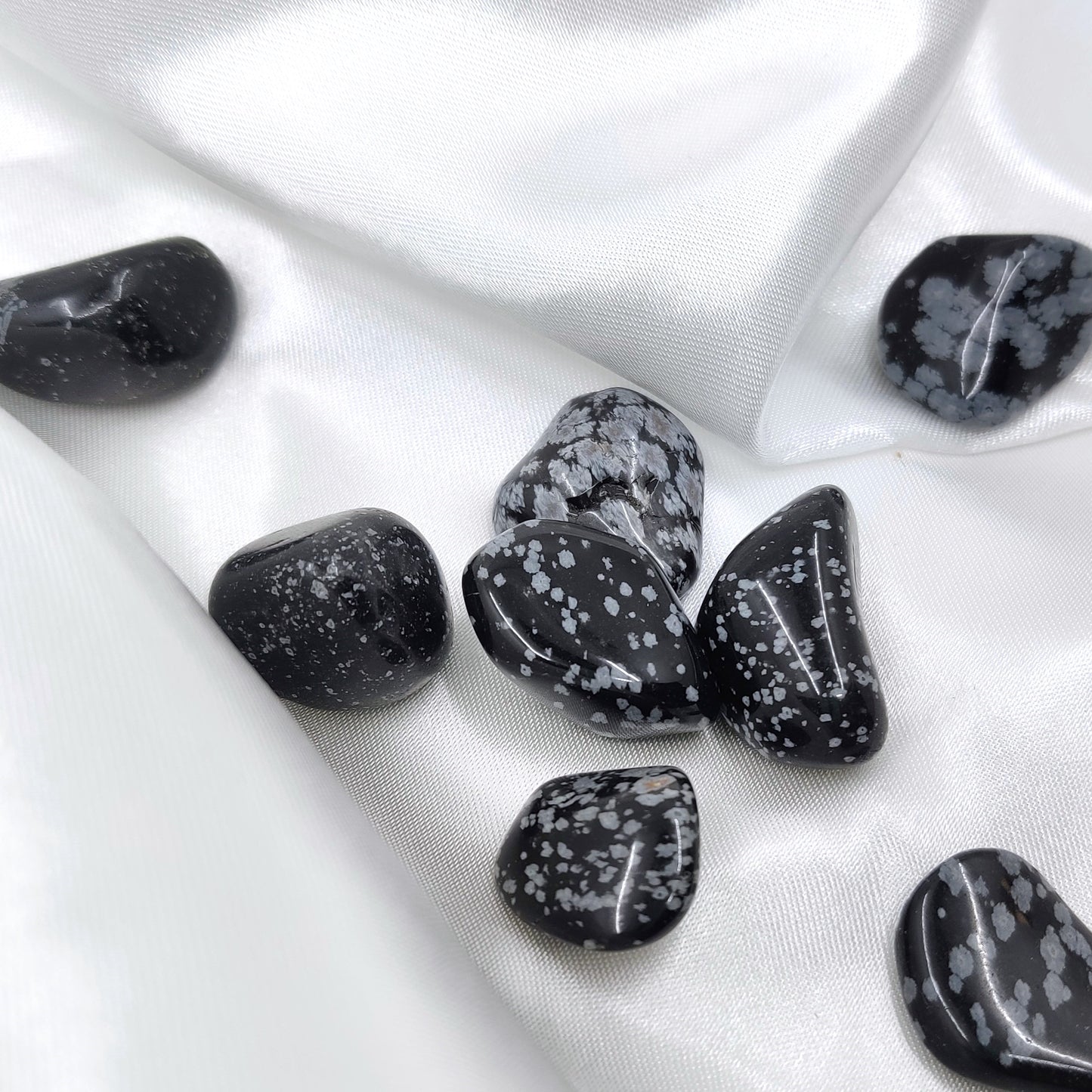 Rumpuhiottuja lumihiutaleobsidiaanikiviä valkoisella silkkikankaalla