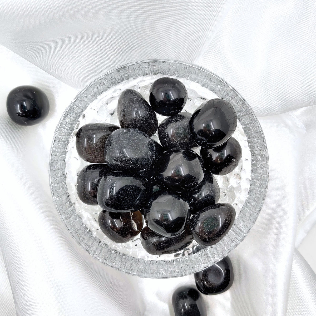 Hiottuja obsidiaaneja lasikulhossa valkoisella silkkikankaalla