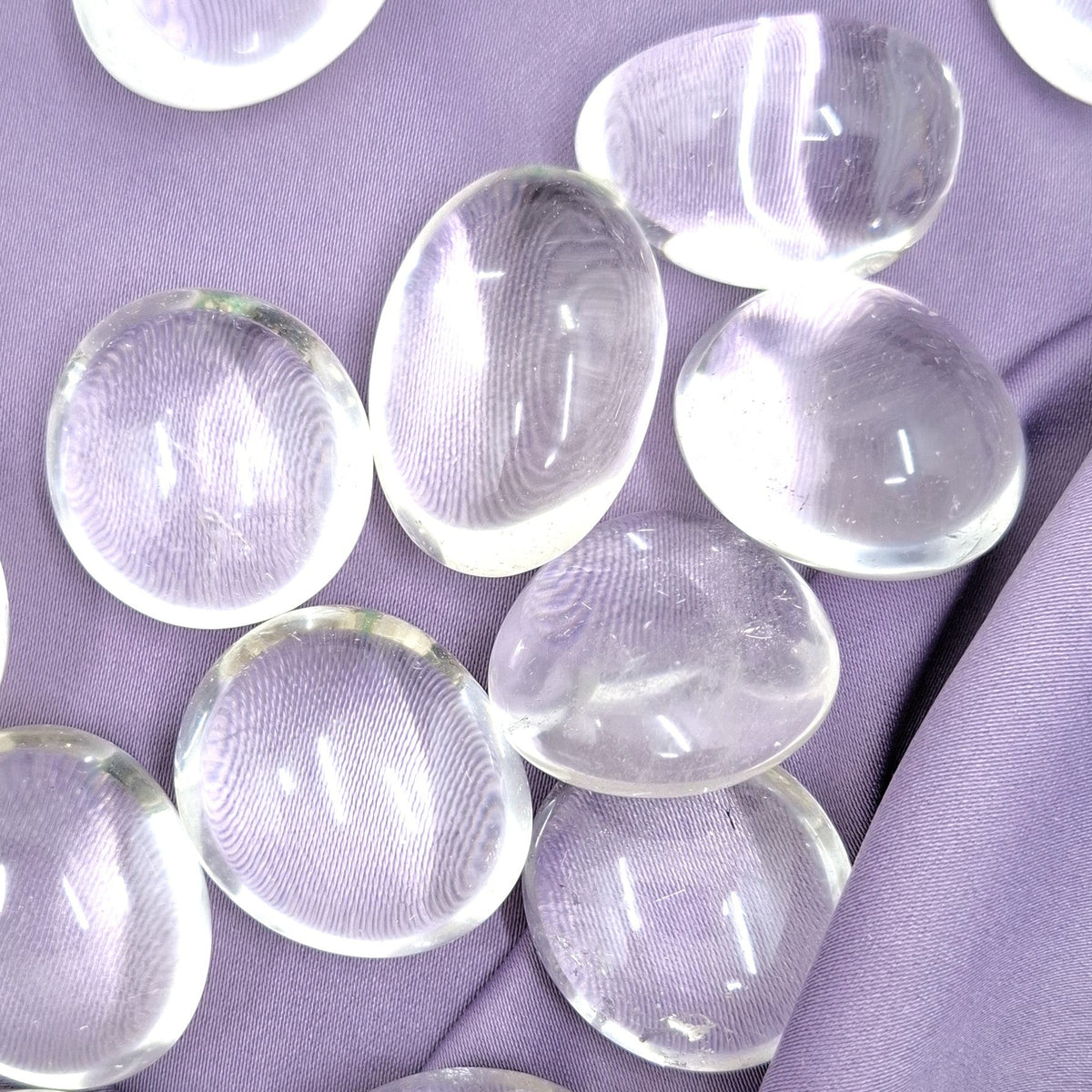 Läpinäkyvät rumpuhiotut vuorikristallit violetilla silkkikankaalla