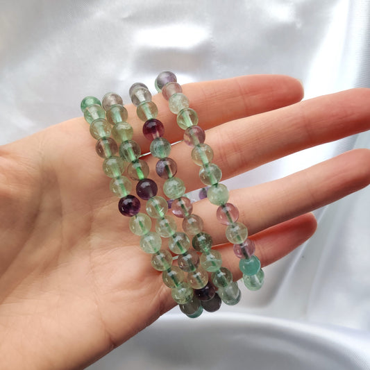 Kiiltävät fluoriitti helmirannekorut käden ympärillä valkoisella taustalla