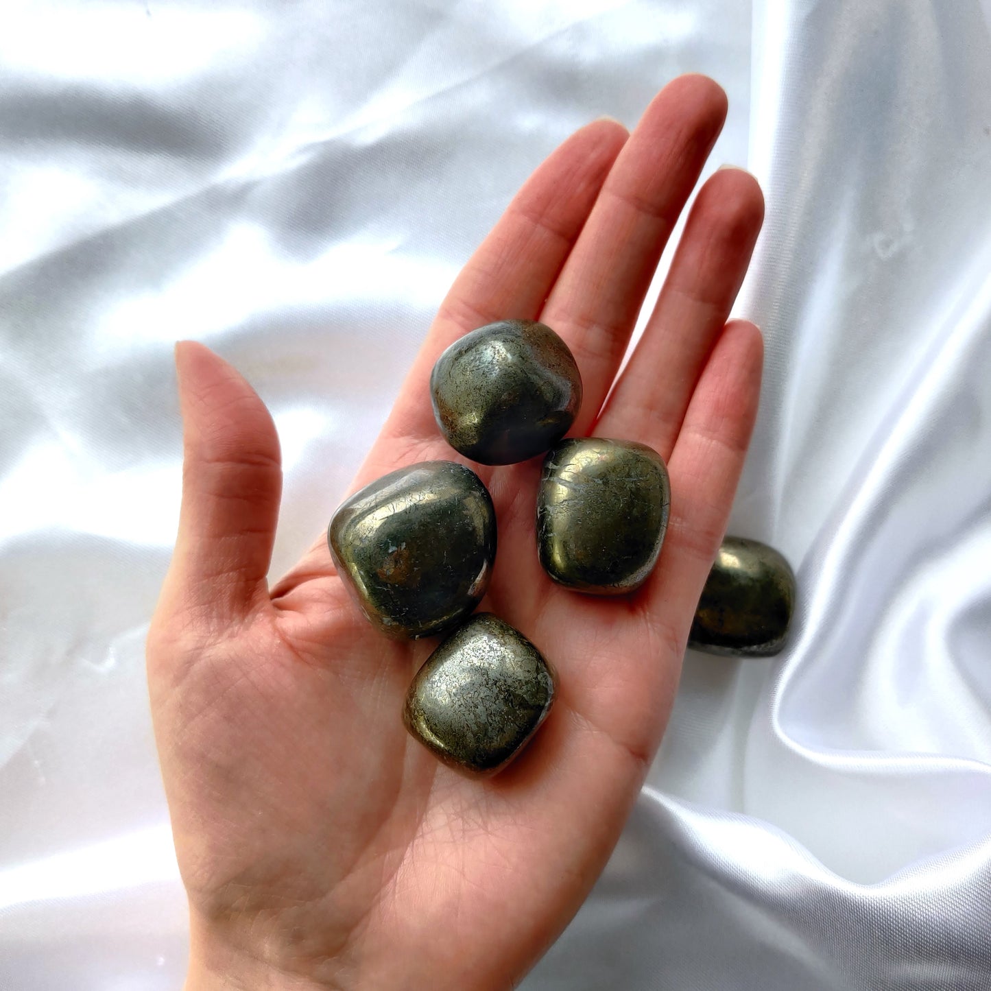 Metallinhohtoiset rumpuhiotut pyriitit kädessä valkoisella taustalla