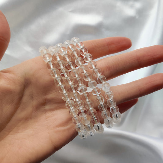 Läpinäkyvät vuorikristalli helmirannekorut käden ympärillä valkoisella taustalla