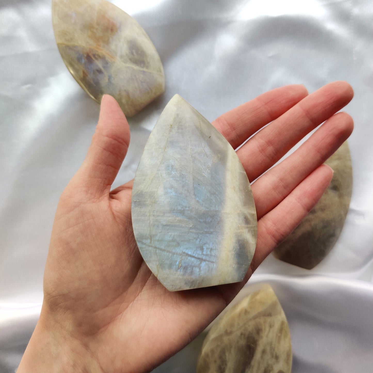 Sinisenä hohtava kuukivipisara kädessä valkoisella pohjalla