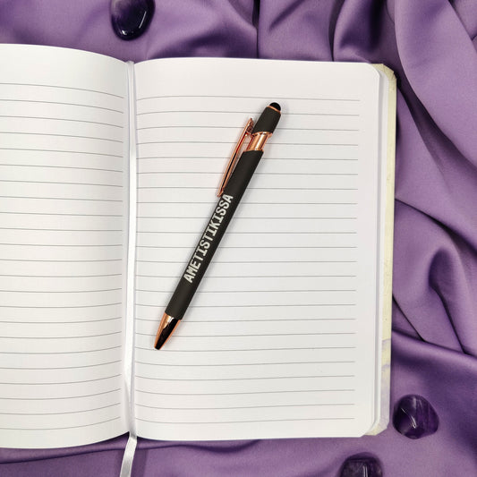 My Book Of Magical thinking muistivihko avattuna, päällä Ametistikissan kuulakärkikynä ja vierellä rumpuhiottuja ametisteja violetilla taustalla