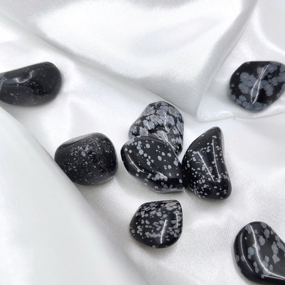 Rumpuhiottuja lumihiutaleobsidiaanikiviä valkoisella silkkikankaalla