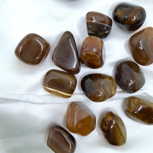 Kiiltävät rumpuhiotut ruskeat akaatit valkoisella kankaalla