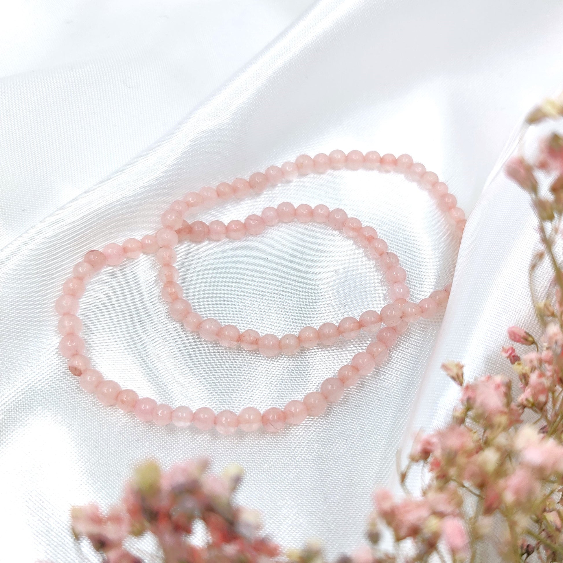 Vaaleanpunaiset ruusukvartsi helmirannekorut valkoisella kankaalla