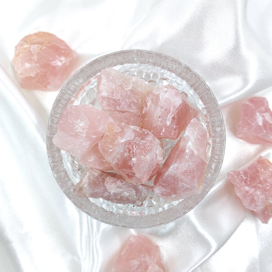 Vaaleanpunaiset ruusukvartsi raakapalat lasikulhossa valkoisella taustalla