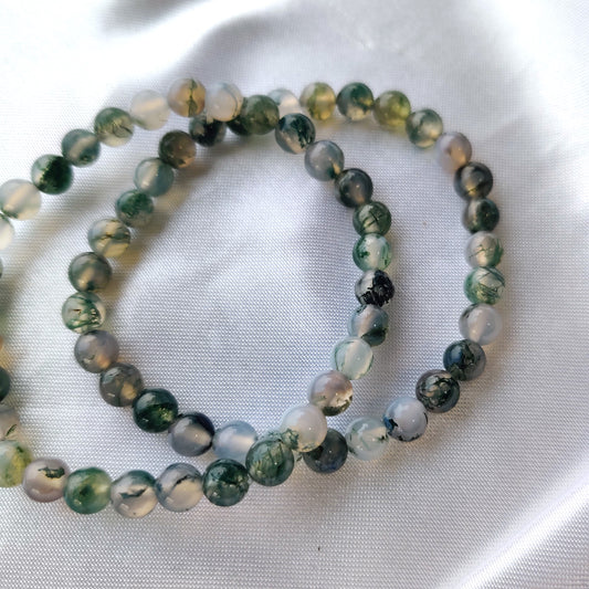 Vihertävät sammalakaattihelmirannekorut valkoisella silkkikankaalla