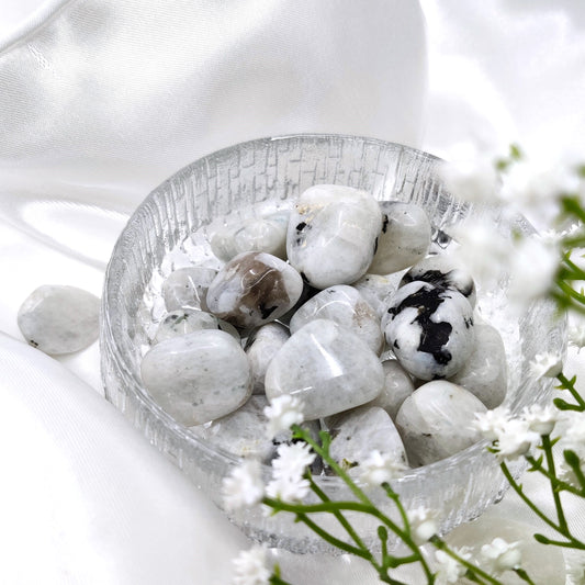 Rumpuhiottuja sateenkaarikuukivikiviä lasikulhossa valkoisella silkkikankaalla