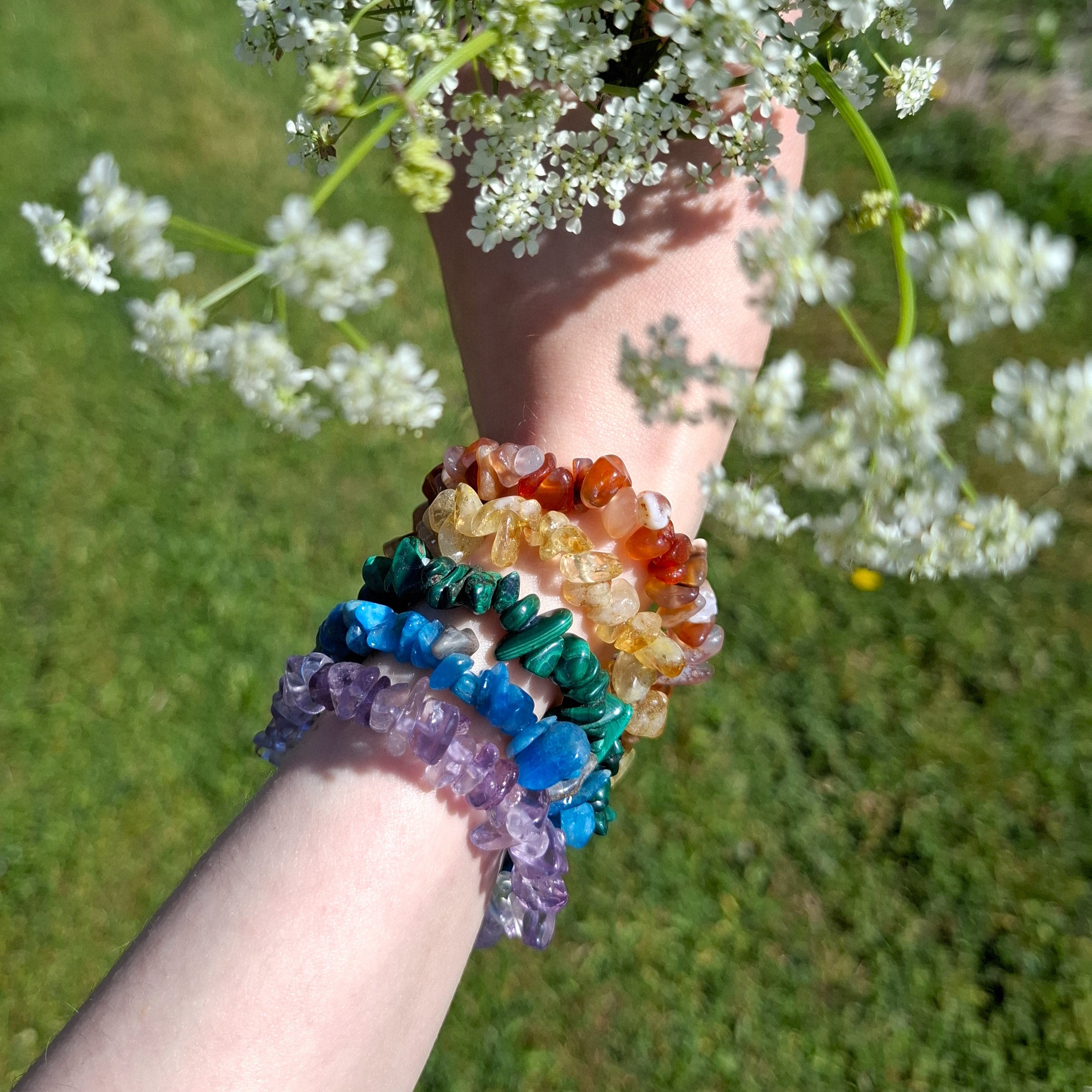 Ametriini, pitsiakaatti, malakiitti, sitriini ja karneolihippurannekorut kädessä kesäisessä kuvassa
