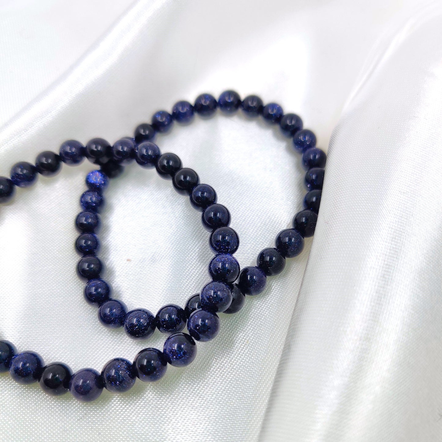 Kimaltavat sininen kultavirta helmirannekorut valkoisella silkkikankaalla