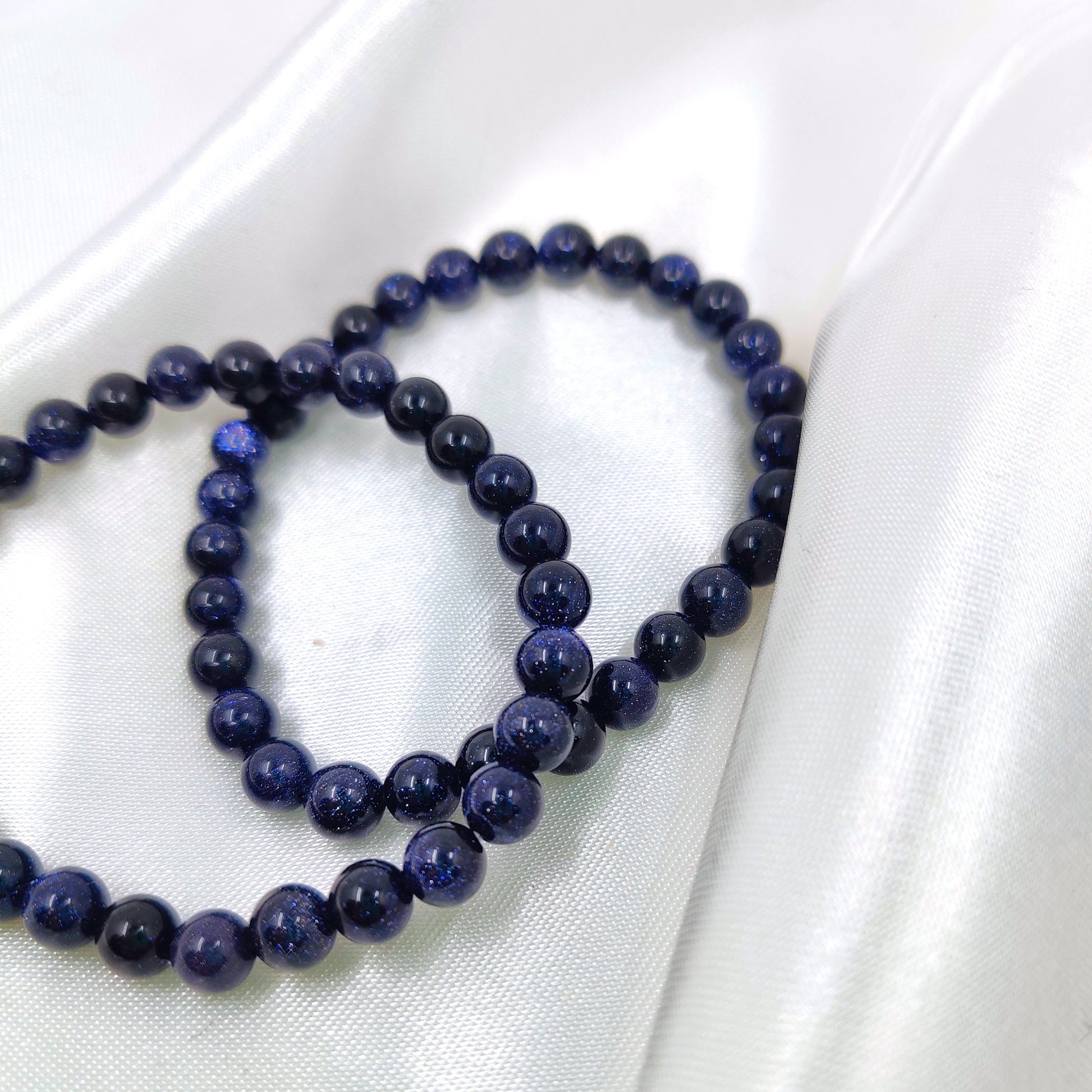 Kimaltavat sininen kultavirta helmirannekorut valkoisella silkkikankaalla