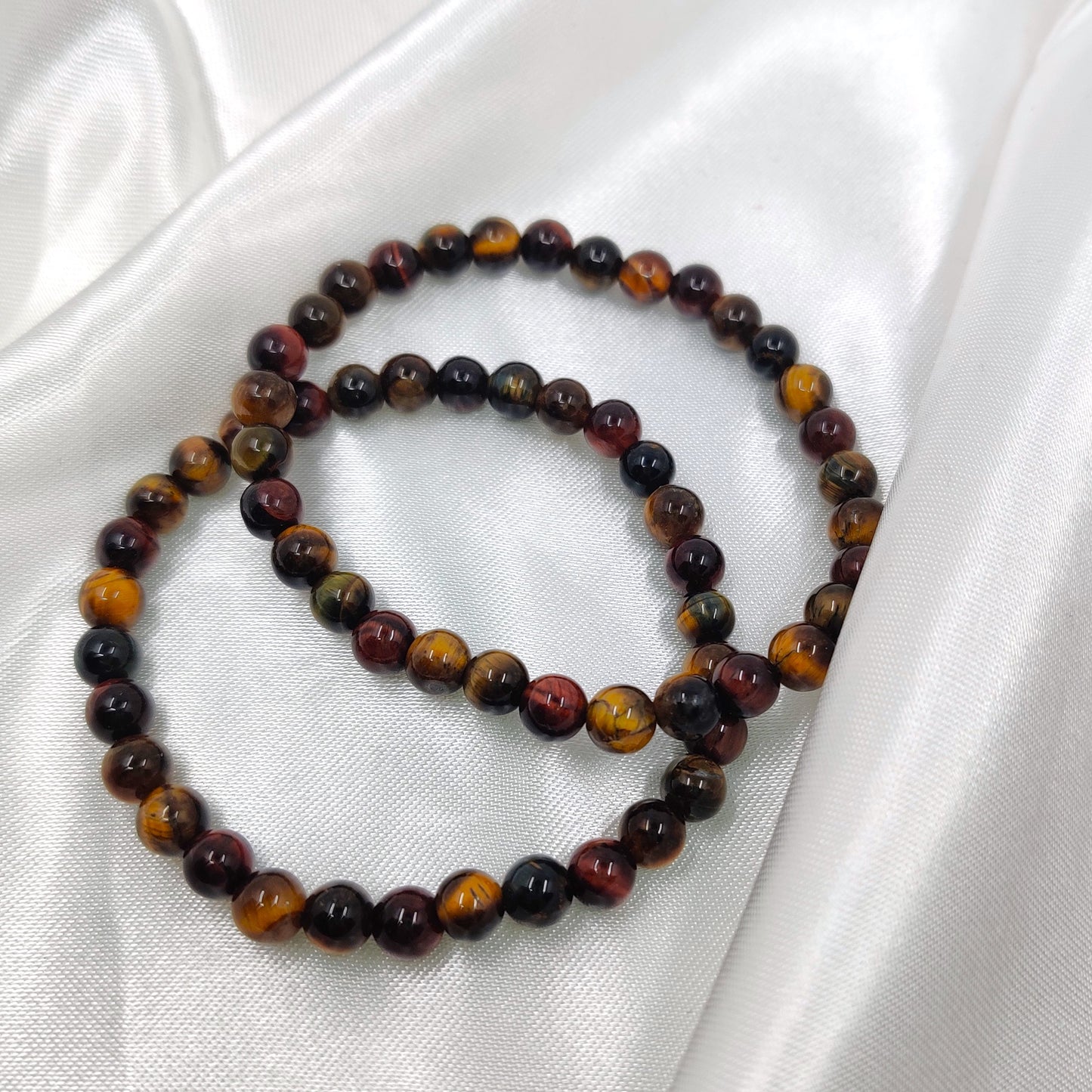 Hohtava tiikerinsilmä mix helmirannekoru valkoisella silkkikankaalla esiteltynä