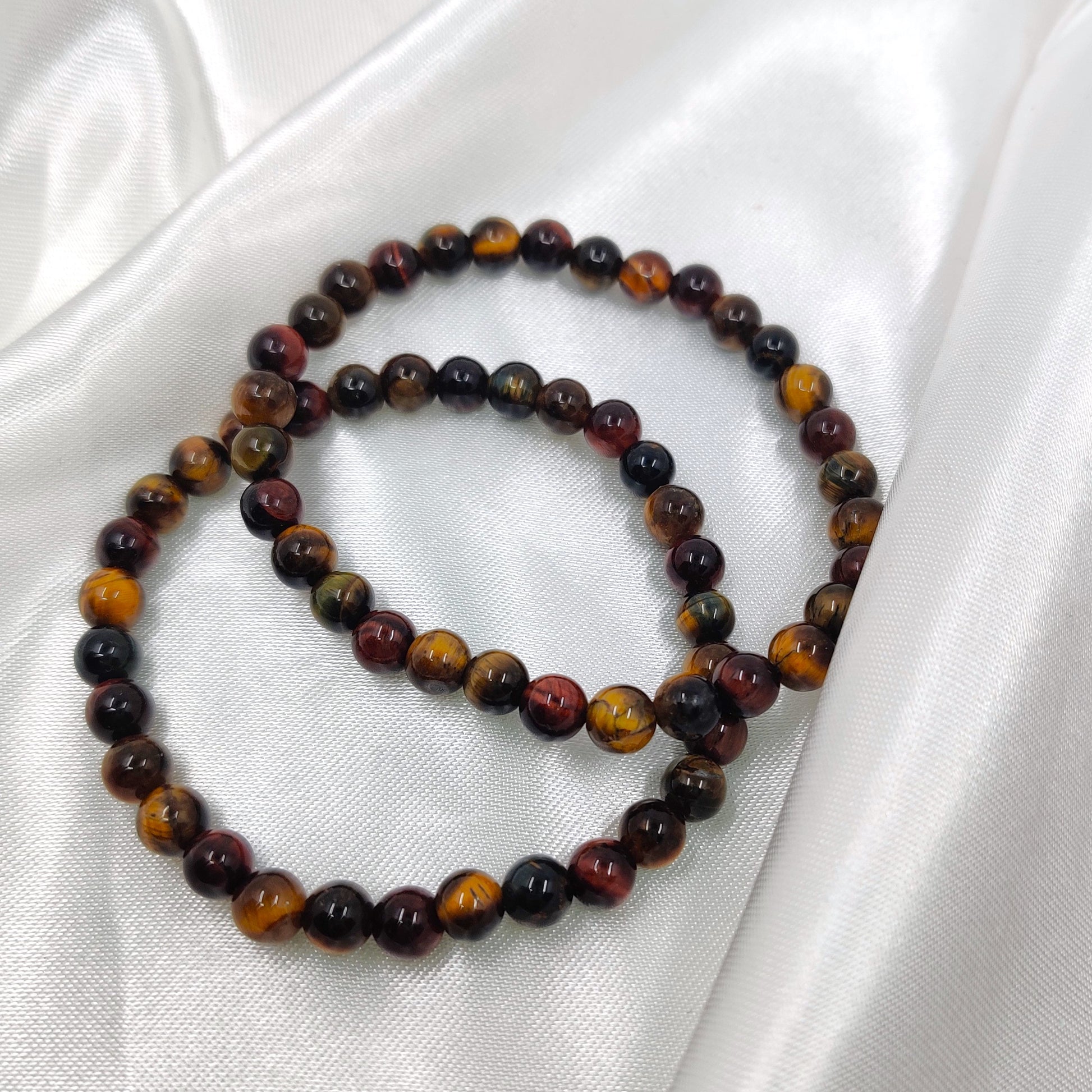 Hohtava tiikerinsilmä mix helmirannekoru valkoisella silkkikankaalla esiteltynä