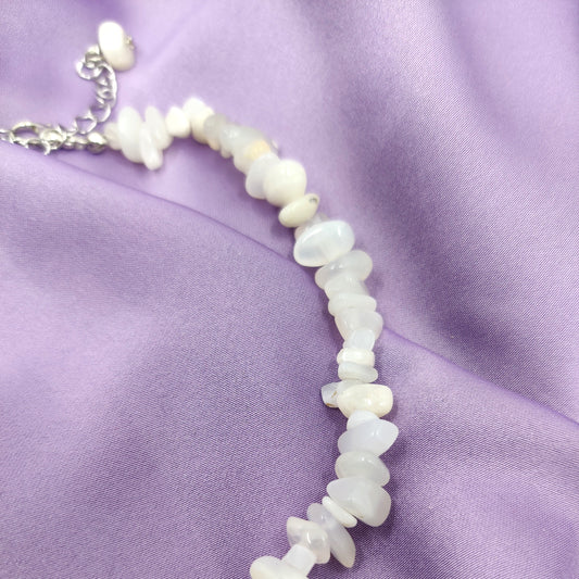 Lähikuva valkoisesta kuukivi hippukaulakorusta violetilla taustalla